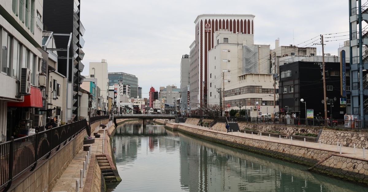 Serene view of a city canal in Fukuoka, Japan, flanked by modern architecture and reflective waters.