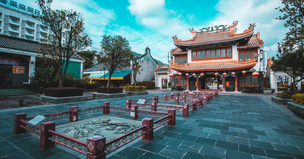 A vibrant view of traditional Chinese buildings in an outdoor plaza with trees and lanterns.