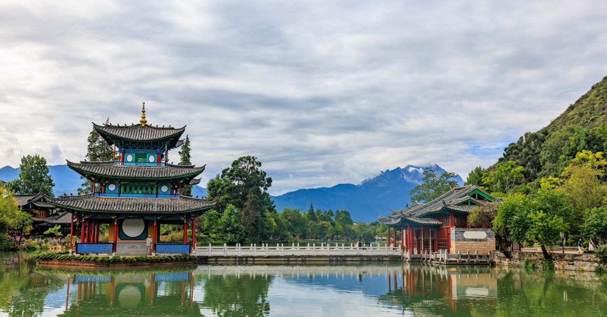 Naxi Hotel, Lijiang — A Stay Addressed on Changshui Road Beautiful Asian architecture reflected in a tranquil lake with mountain backdrop.
