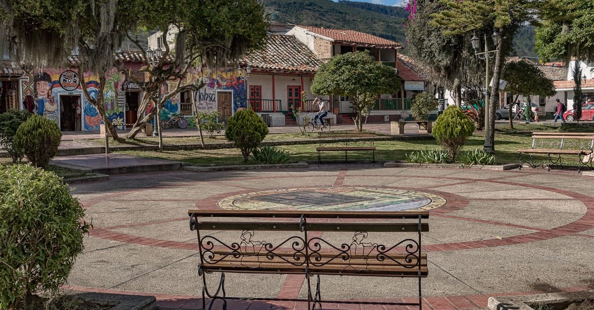 Peaceful town square with benches, art murals, trees, and historic buildings on a sunny day.