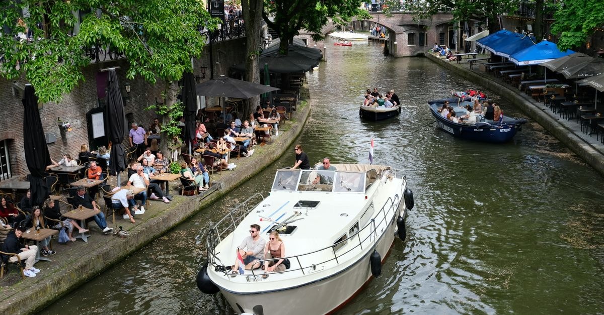 A slow-travel Utrecht travel guide for canal-side wanderers Vibrant scene of boats navigating Utrecht canal, flanked by bustling cafes.