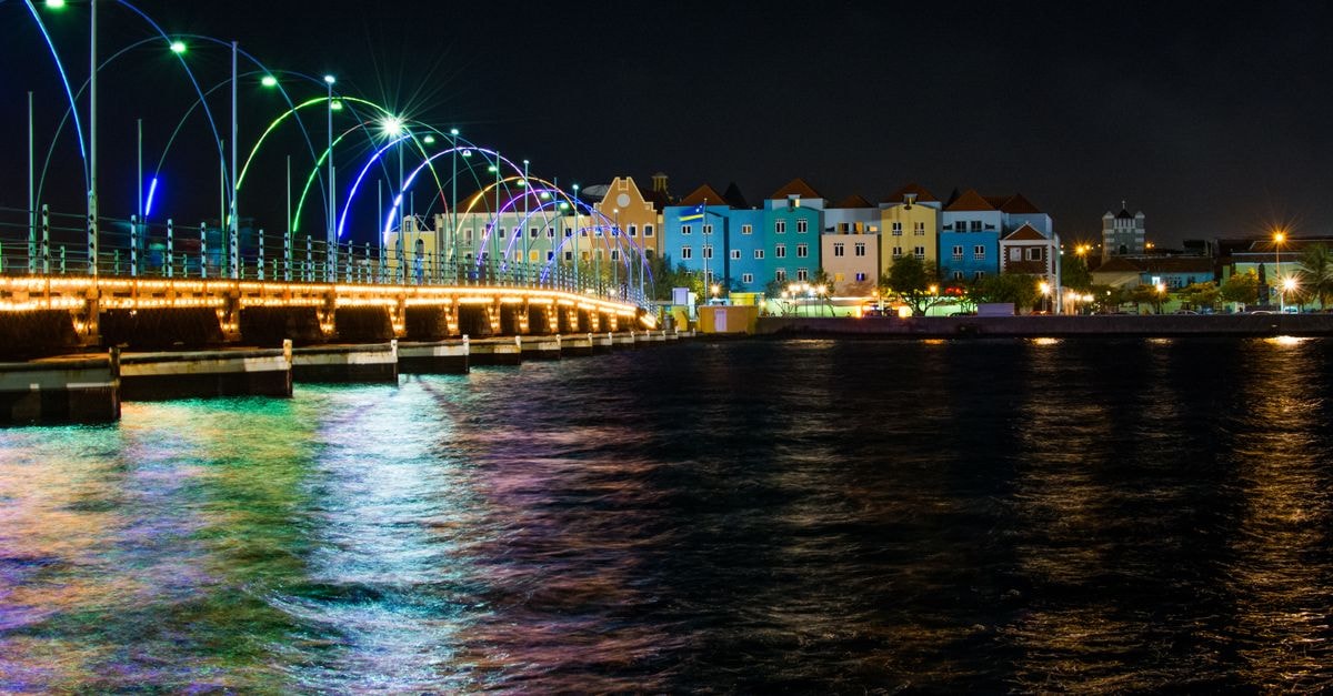 Vibrant night view of the Queen Emma Pontoon Bridge in Curacao with colorful lights and waterfront reflection.
