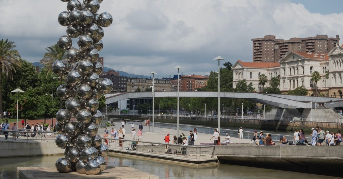 Bilbao Travel Guide: Where Avant-Garde Architecture Meets Basque Tradition A modern sculpture by the river in Bilbao, Spain, featuring shiny spheres with a city backdrop.