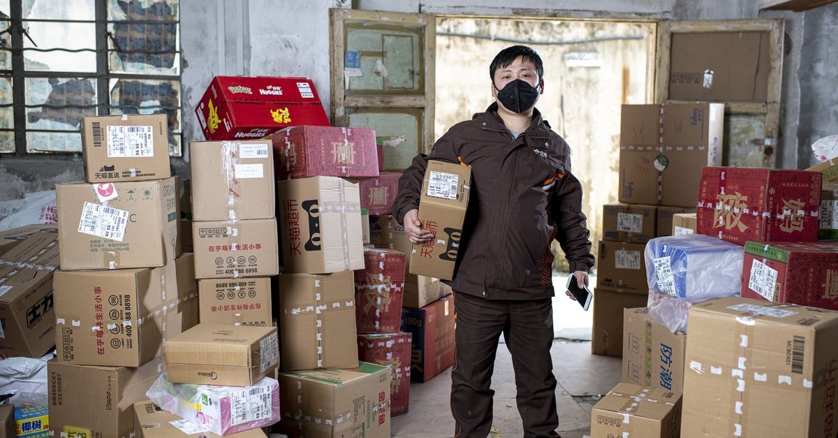 The Home Depot: Premium Multiple Meets Housing-Cyclical Cash Engine Delivery worker holding packages in a Wuhan warehouse, wearing a face mask.