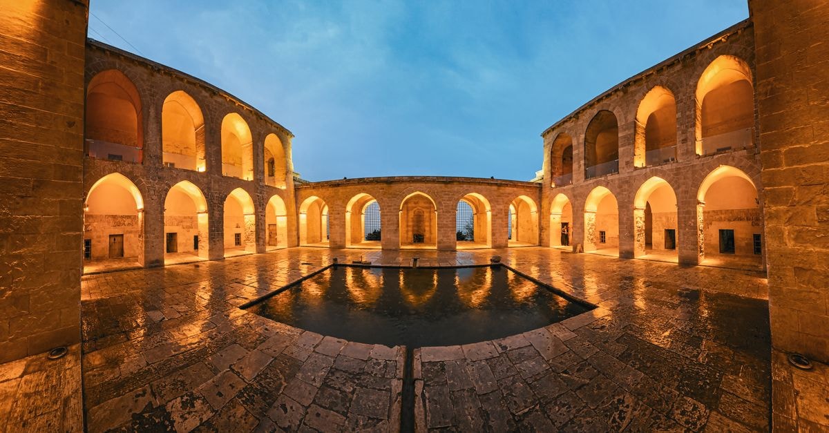 Sanliurfa Travel Guide: Walking an Ancient City in Upper Mesopotamia Beautiful courtyard in Mardin, Türkiye, at dusk with warm lighting and reflections in the water.