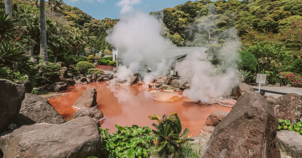 APA Hotel Beppu Ekimae in Beppu: One-Minute Walk from the Station Explore a vibrant hot spring surrounded by lush greenery with rising sulfur smoke under a clear blue sky.