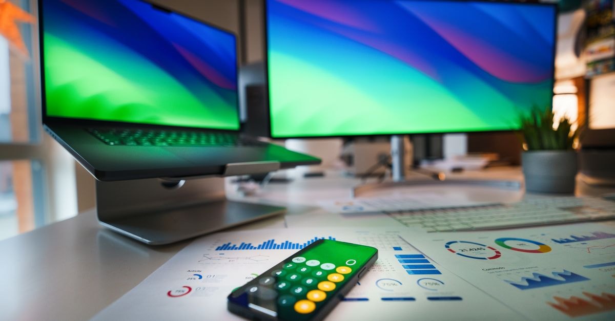 Contemporary office desk featuring a laptop, smartphone calculator app, and business graphs.
