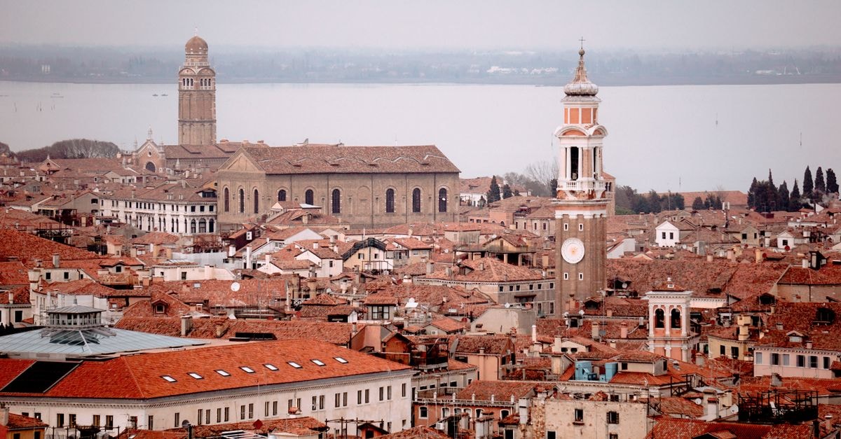 Hotel San Luca, Venice: A Two-Building Stay in the Historic Heart Panoramic aerial view of Venice showcasing red rooftops, towers, and historic architecture under a cloudy sky.