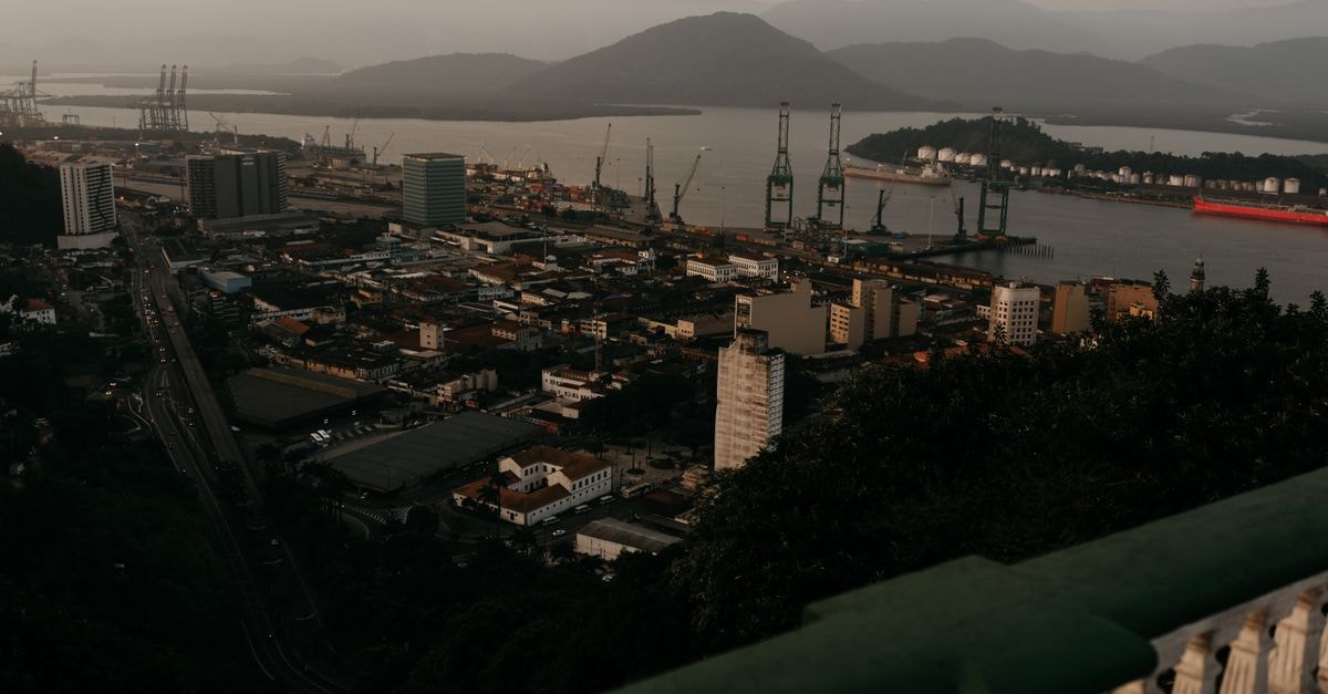 High angle of port of coastal town with cargo cranes and houses on river shore