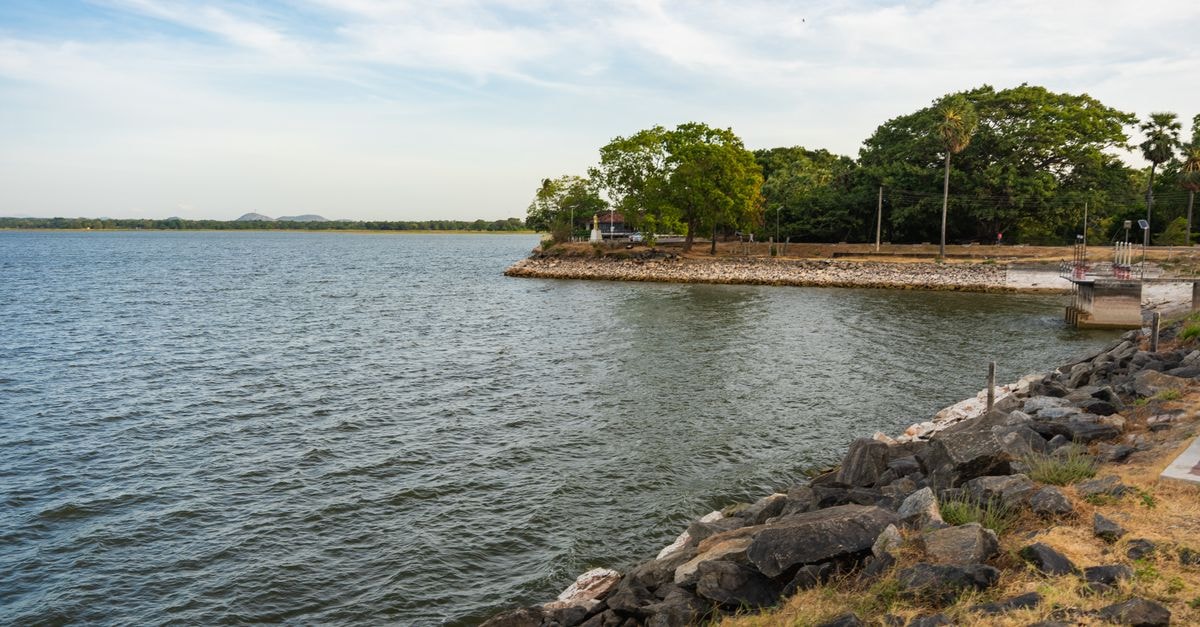 Scenic view of lake with rocky shoreline and lush greenery in Polonnaruwa, Sri Lanka.