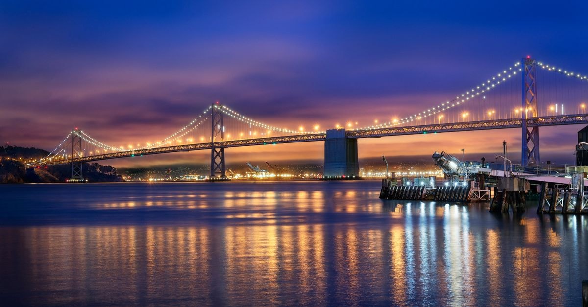 The Oakland Bay Bridge brilliantly lit over calm waters during twilight in San Francisco.