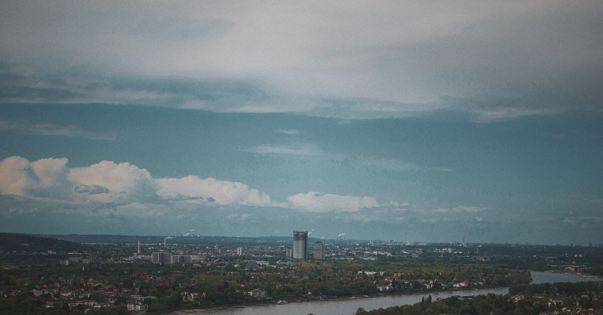 Hilton Mainz in Mainz: Rhine Views by the Old Town A breathtaking aerial view of a modern cityscape featuring a meandering river under a dramatic cloudy sky.