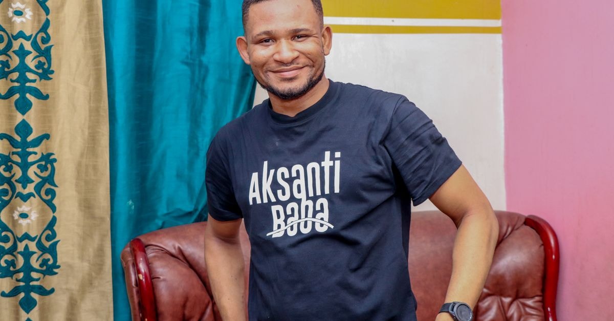 A cheerful man smiles warmly while posing indoors in Kinshasa, vibrant colors around.
