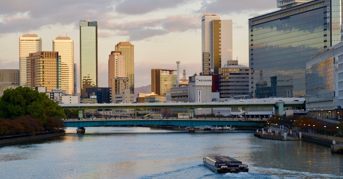 U Community Hotel in Osaka: An Event-Ready Stay in Higashiōsaka Scenic view of Osaka skyline and river during a calm day. Reflective high-rises and tranquil water create a serene atmosphere.
