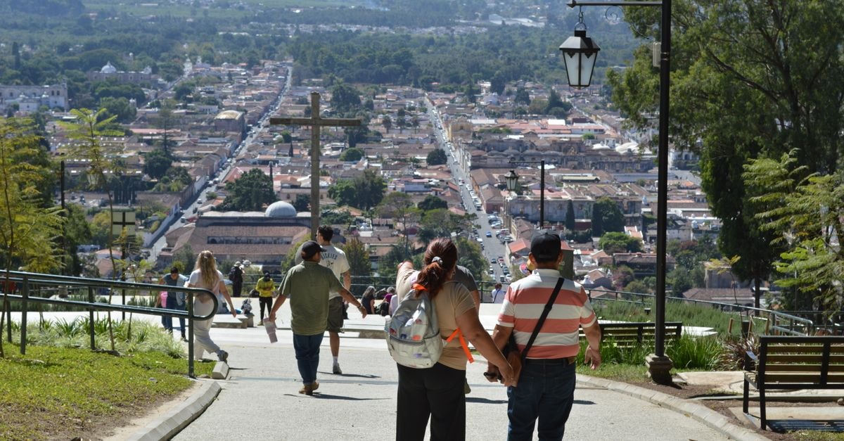 A couple holding hands while walking down a path overlooking a scenic cityscape.
