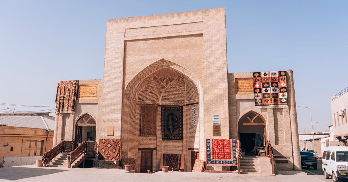 Margilan Travel Guide: Silk Workshops and Fergana Valley Charm Historic building in Bukhara showcasing Uzbek carpets and textiles under a clear sky.
