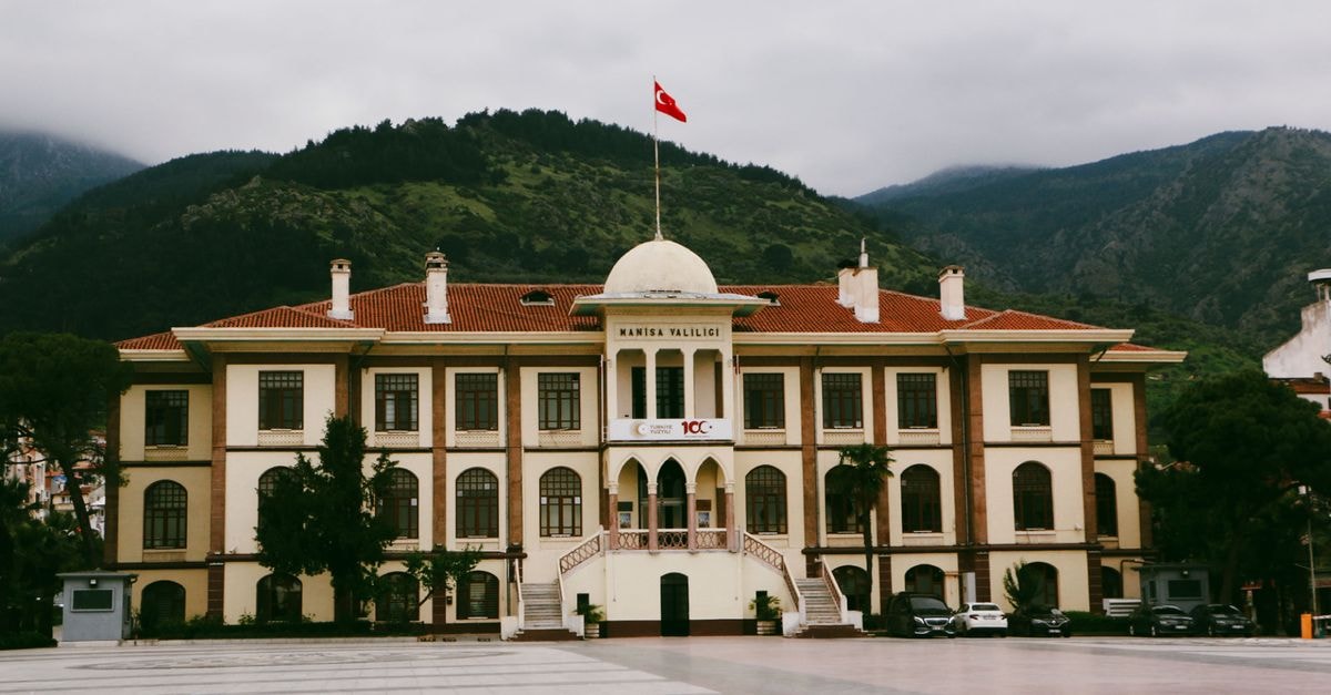 Government building in Manisa, Turkey with mountainous backdrop and Turkish flag.