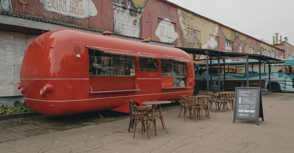 Red food truck with tables in a colorful urban environment with graffiti walls.