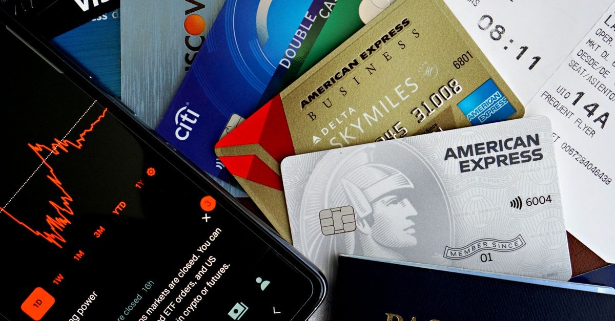 American Express launches next-generation Amex Corporate program with new Cashback Card and expense tools Flat lay of credit cards, passport, and a phone showing stock data, depicting finance and travel.
