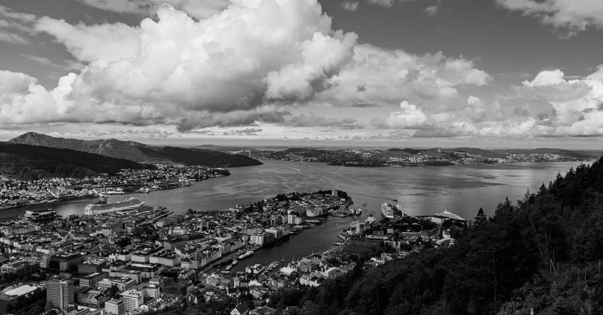 A breathtaking black and white aerial view of Bergen cityscape and coast under dramatic clouds.