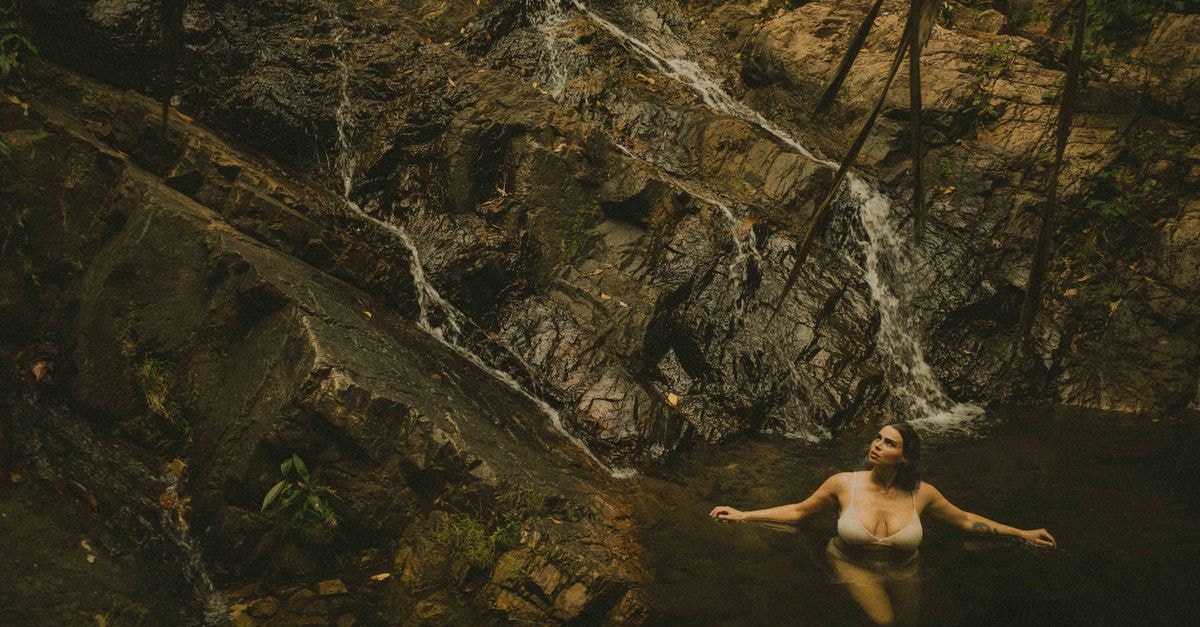 Coamo Travel Guide: Hot Springs and Slow South-Central Puerto Rico A woman enjoys a peaceful moment in a natural waterfall pool surrounded by rocky terrain.