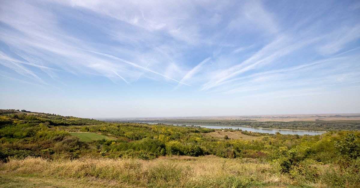 Ungheni Travel Guide: Crossing Points and Quiet Moldova Days A vast countryside landscape featuring rolling hills, green fields, and a river under a bright blue sky with clouds.