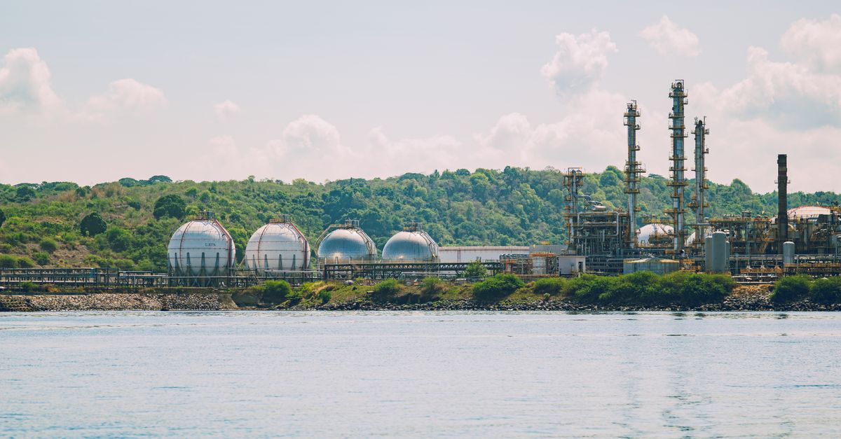 A scenic view of a coastal industrial gas storage facility with spherical tanks and tall chimneys.