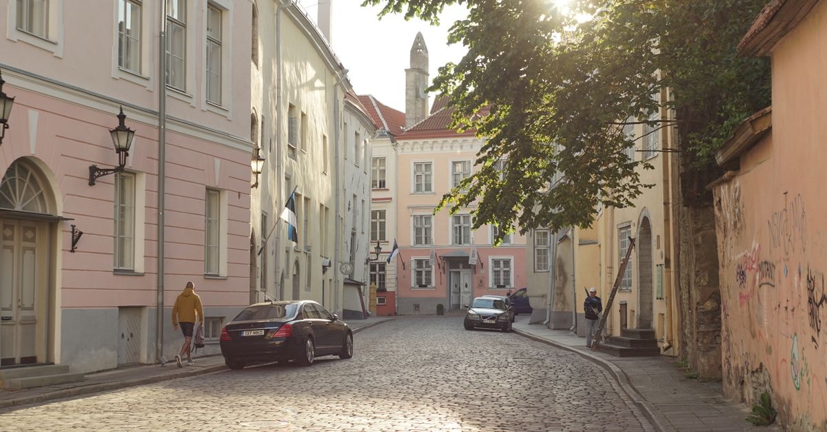 Charming cobblestone street in European city during sunrise, featuring historic buildings and parked cars.