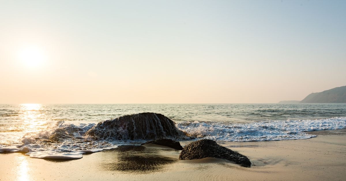 Mangaluru travel guide: coastal calm and coastal flavour Peaceful beach view with rocks and gentle waves under a warm sunset sky.