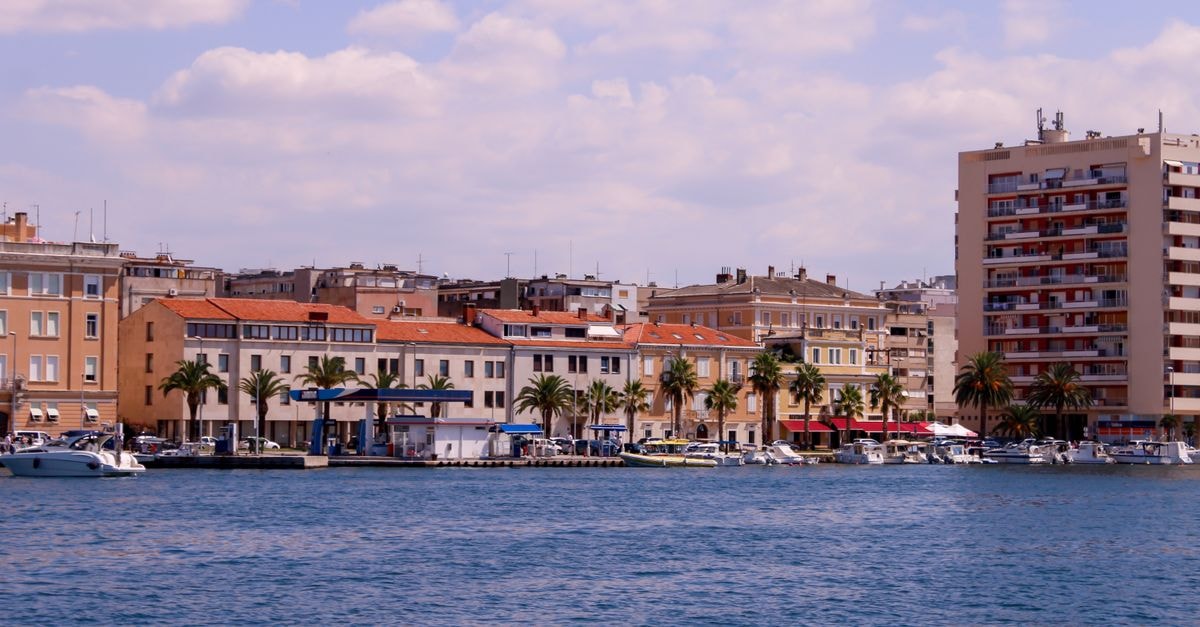 A beautiful cityscape featuring waterfront buildings and palm trees under a clear summer sky.
