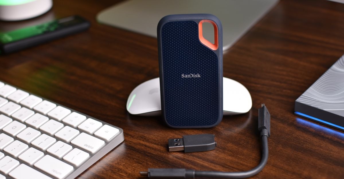 SanDisk 股價滑落,AI 放緩警告引發記憶體拋售潮 SanDisk 可攜式 SSD 搭配 USB 線與電腦配件置於木桌上。