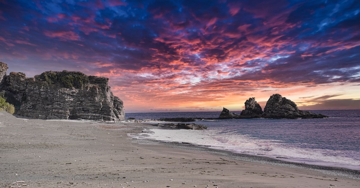 Vibrant sunset over Άρβη beach with dramatic sky and calm seas, Greece.