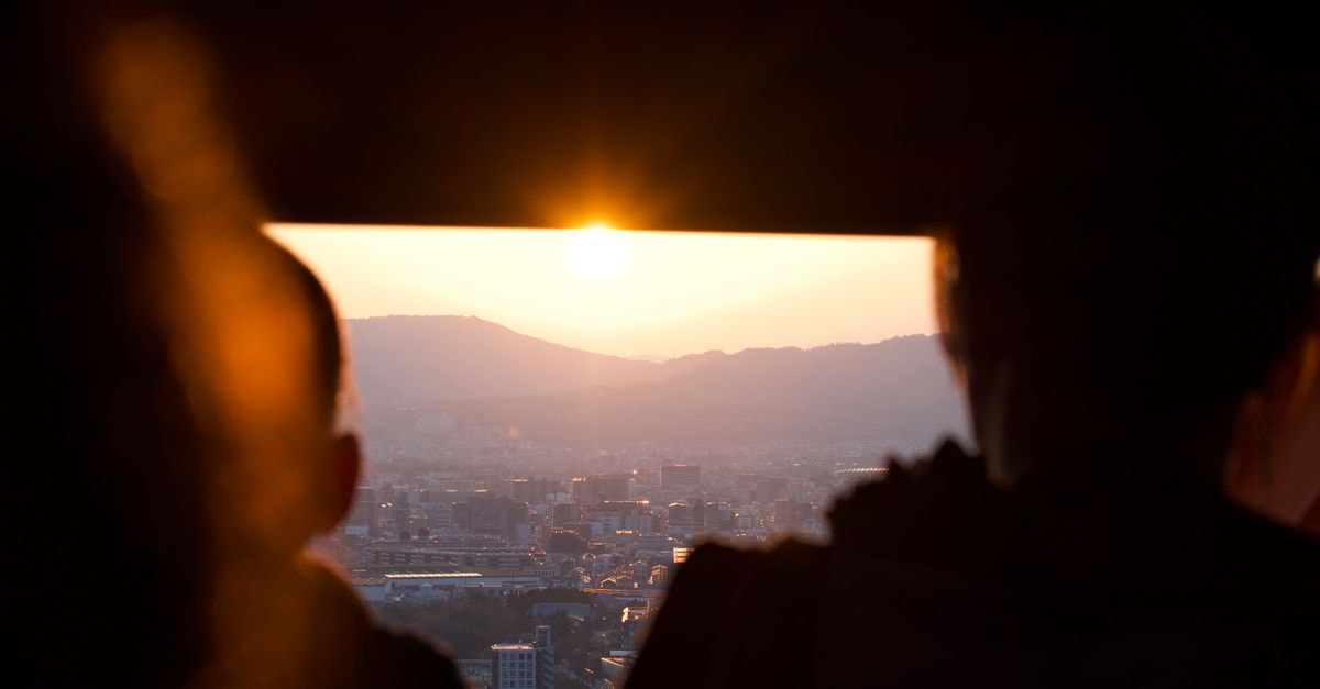 Ramada by Wyndham Jeonju in Jeonju: Skyline Cocktails on Level 15 Silhouettes of two people watching a vibrant sunset over a sprawling cityscape and mountains.