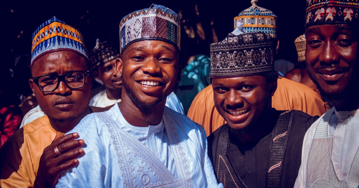 Sokoto Travel Guide: Caliphate Heritage and Northern Nigeria Charm A cheerful group of Nigerian men wearing colorful traditional attire and caps, outdoors.
