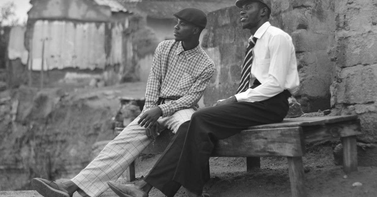 Two men sitting on a bench in Sekondi-Takoradi, Ghana, in a vintage black and white style.