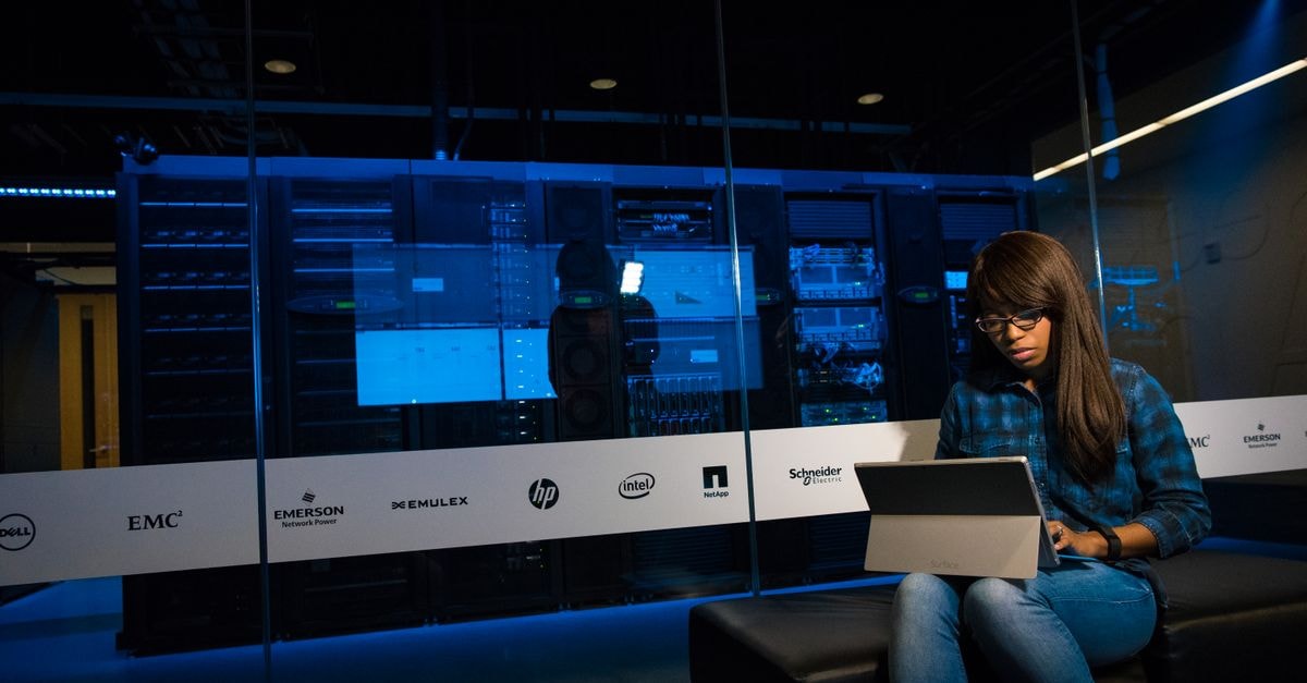 Broadcom Is Raising Up To $100 Billion in Fresh Debt to Finance AI Chip Deals Woman using a laptop in a server room, showcasing modern technology and work environment.