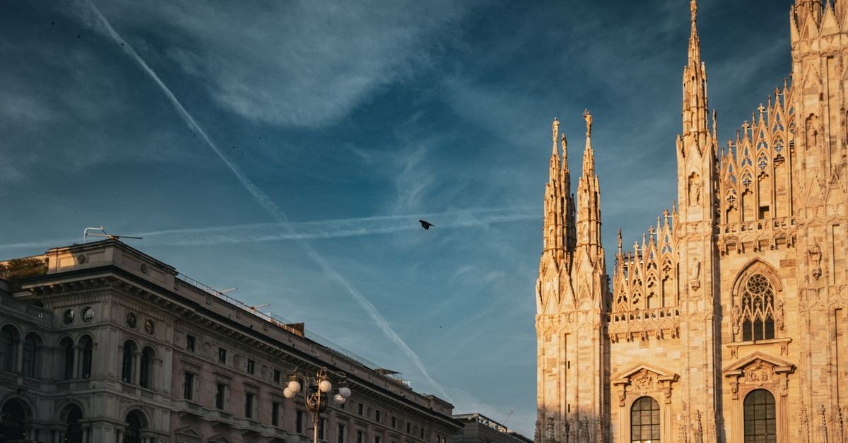 Milan travel guide: art, aperitivo and Lombard rhythm Captivating evening shot of the Milan Cathedral with clear skies and birds in flight, capturing its intricate Gothic architecture.