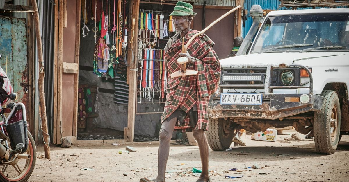 A traditional Kenyan scene featuring a local musician playing an instrument on a street in Kenya, with vibrant market goods.