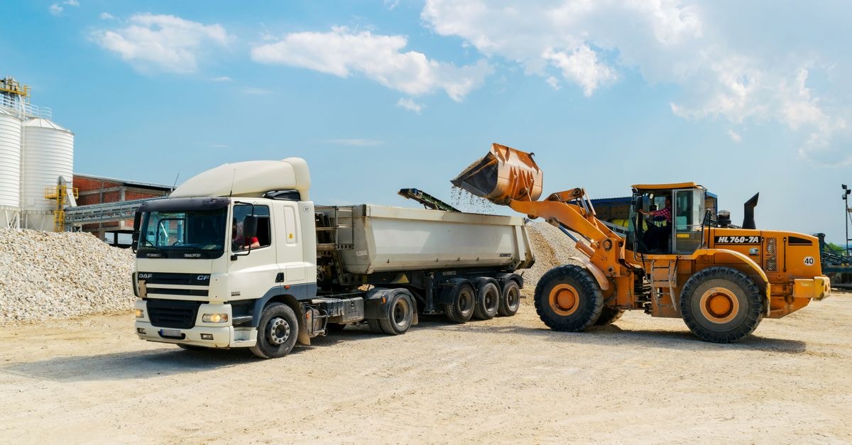 Blue Bird Corporation: A School-Bus Franchise Tested by Acquisition Math Excavator loading materials into a heavy-duty truck at a sunny construction site.