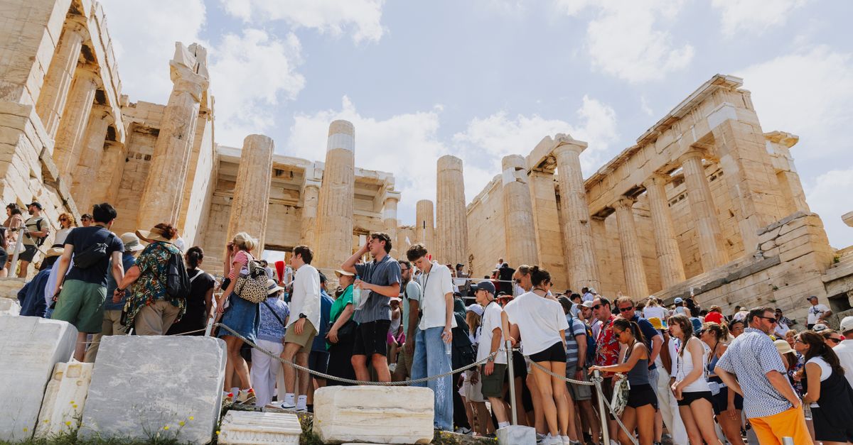 A crowded scene of tourists exploring the ancient ruins at the Acropolis in Athens, Greece.
