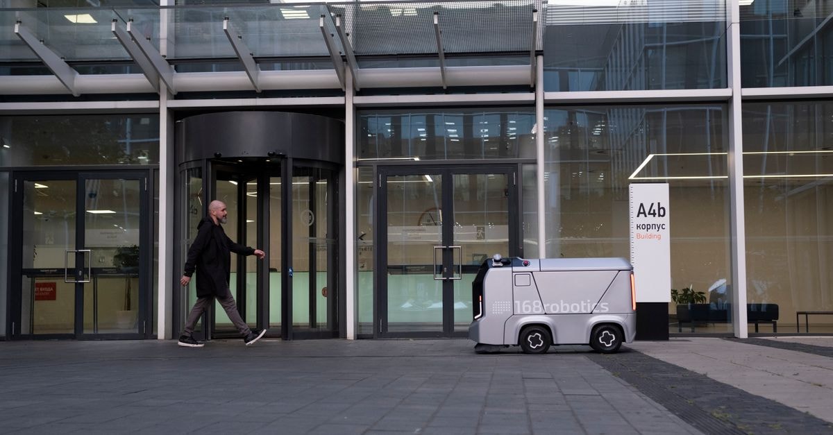 A modern office setting featuring a man and an autonomous delivery robot outside a glass-covered building.
