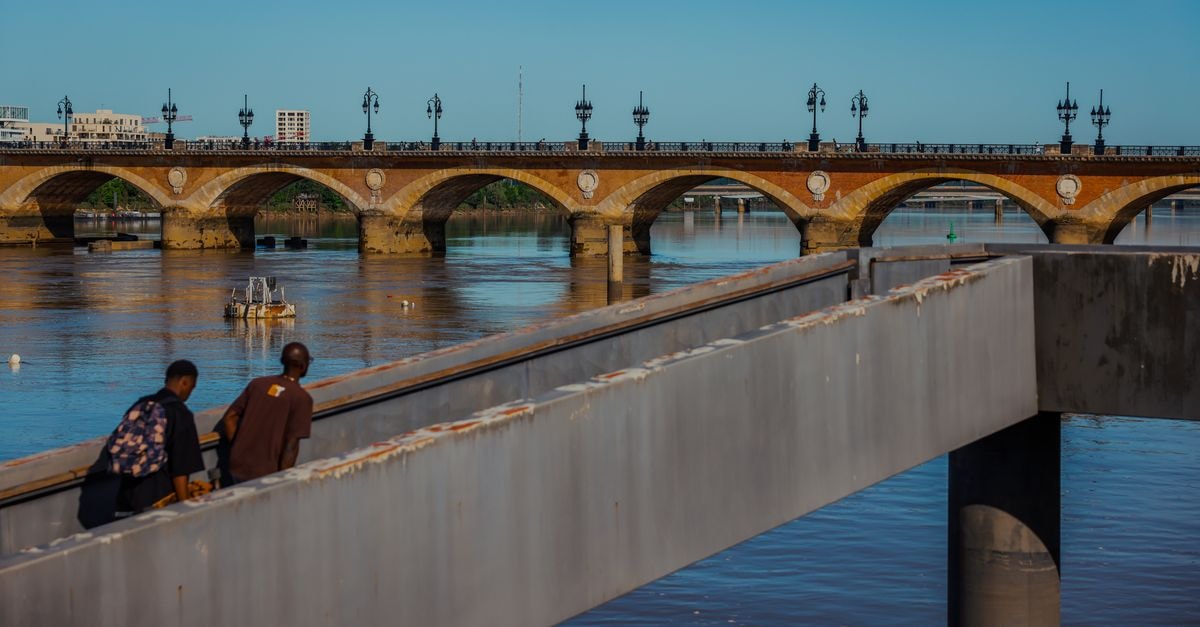 View of the historic Pont de Pierre bridge in Bordeaux, spanning the Garonne River with people in the foreground.