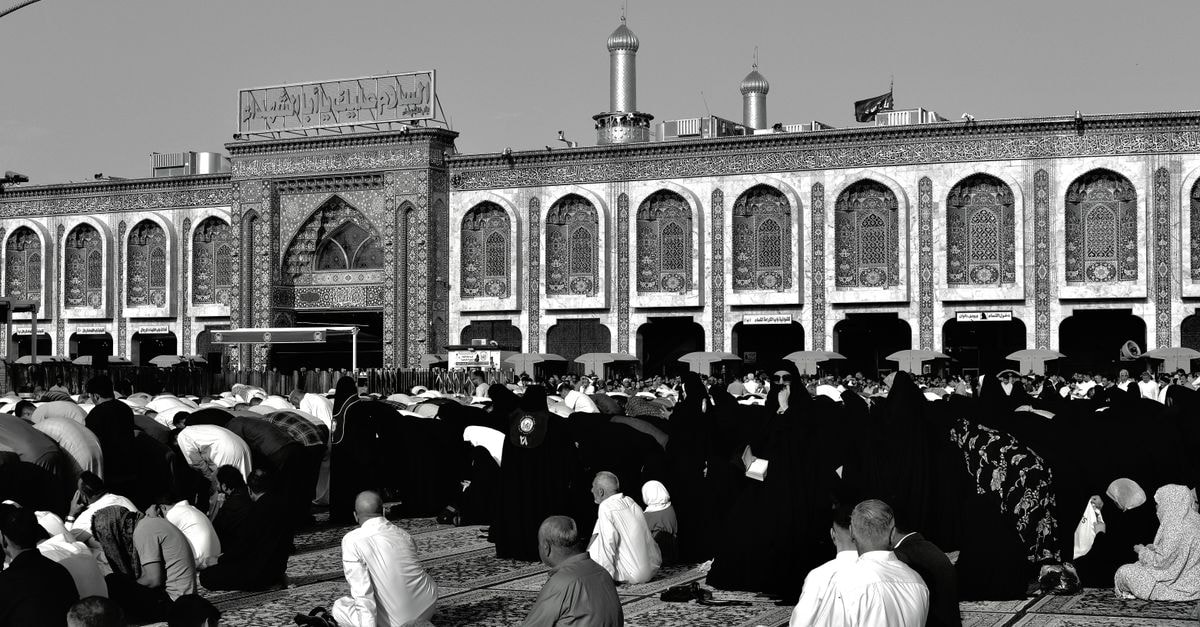 Mashhad Travel Guide: Pilgrimage Routes and Practical City Tips Black and white image of people praying outside a mosque in Karbala, Iraq.