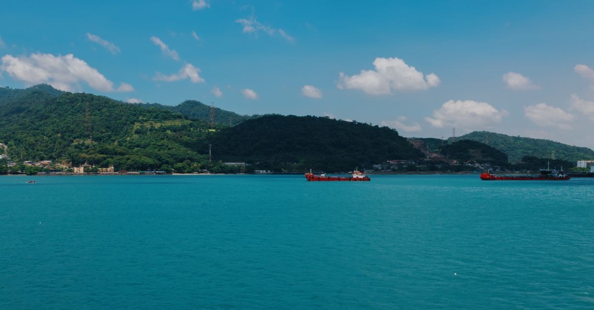 Dumai travel guide: harbor charm on Indonesia's Riau coast A vibrant view of cargo ships on the turquoise sea against Indonesia's lush coastline.
