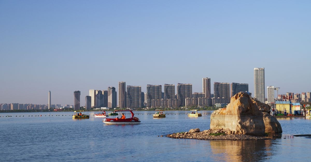 Deyang Hotel in Deyang: An Industrial Hub Near Ancient Sanxingdui Roots View of a contemporary city skyline with boats on a clear blue waterfront.