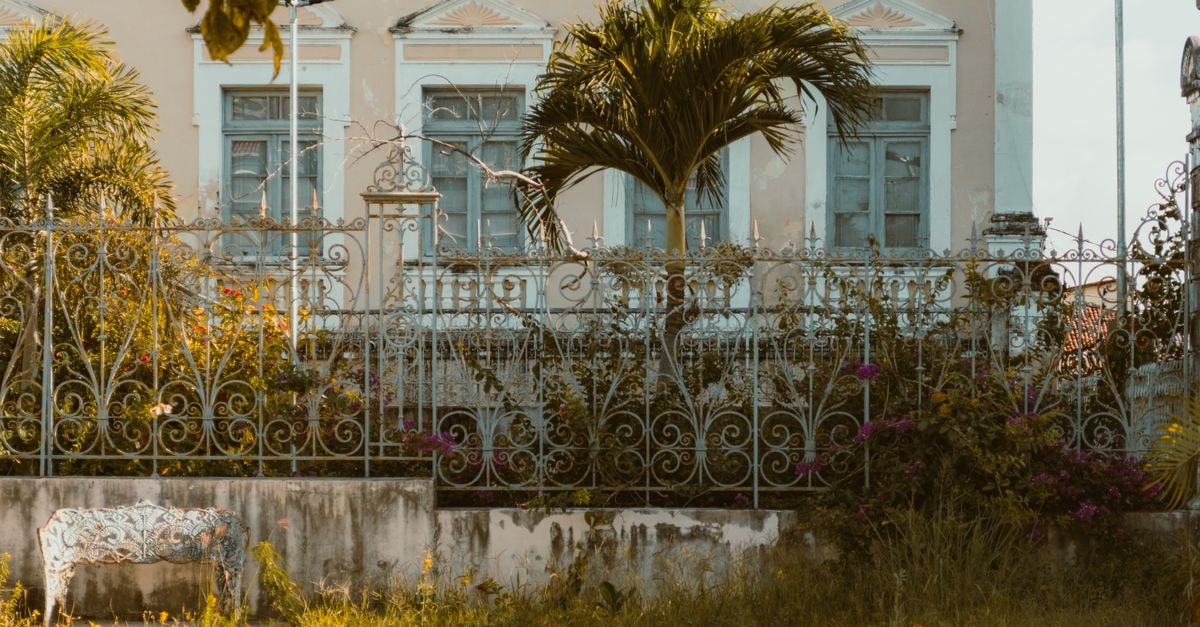 A colonial-style house facade with lush greenery and palm trees in Natal, Brazil during the day.
