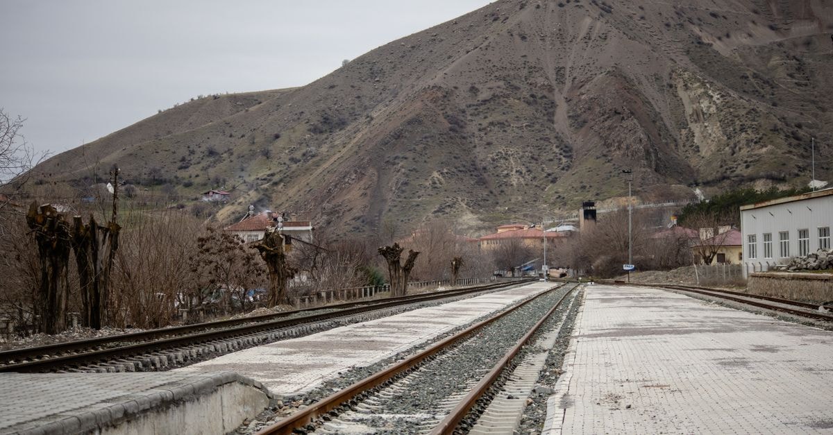 Railway tracks stretch through Palu, Türkiye with a backdrop of bare hills under a cloudy sky.