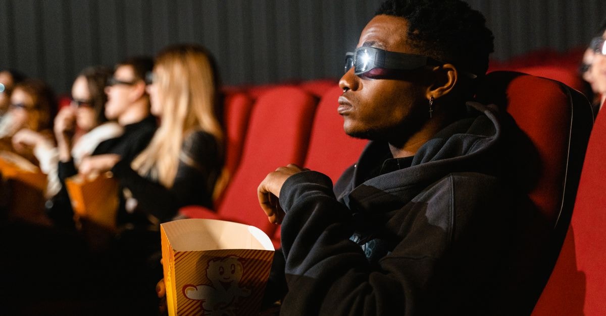 A group of adults in a cinema wearing 3D glasses watching a movie and eating popcorn.