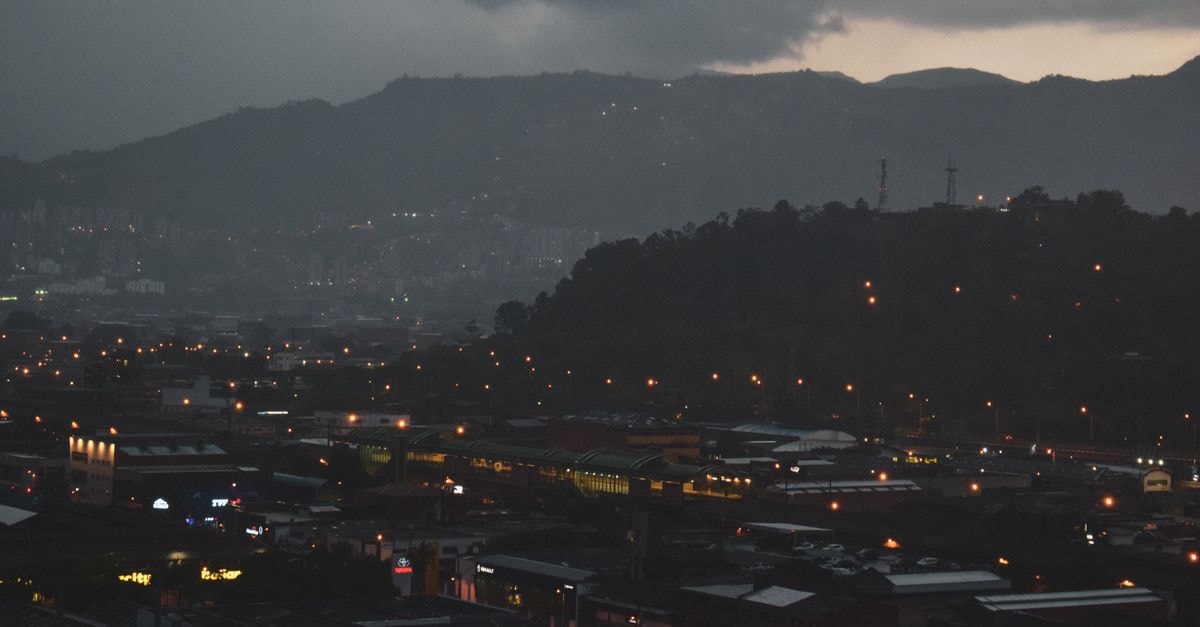 Mirador Andino, Manizales — A Family Hostal Across from Parque Fundadores Aerial view of an urban cityscape at night with glowing lights and distant mountains.
