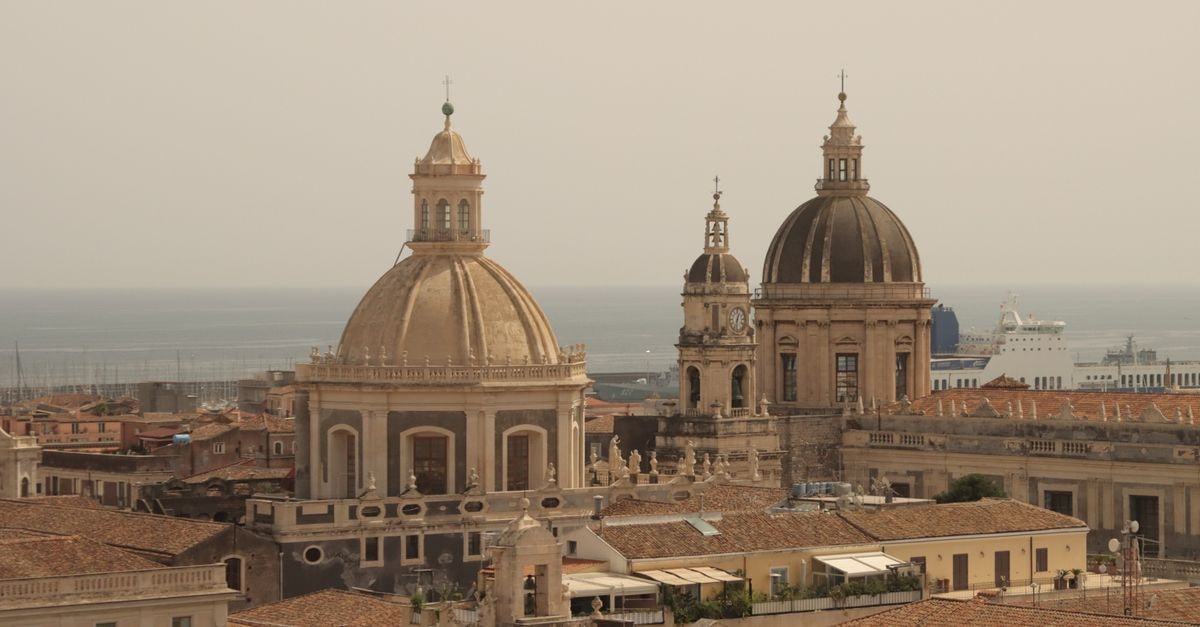 Ploes Boutique Hotel in Ermoupoli: A 150-Year Neoclassical Mansion Impressive aerial shot of Catania Cathedral domes overlooking the sea in Sicily, Italy.